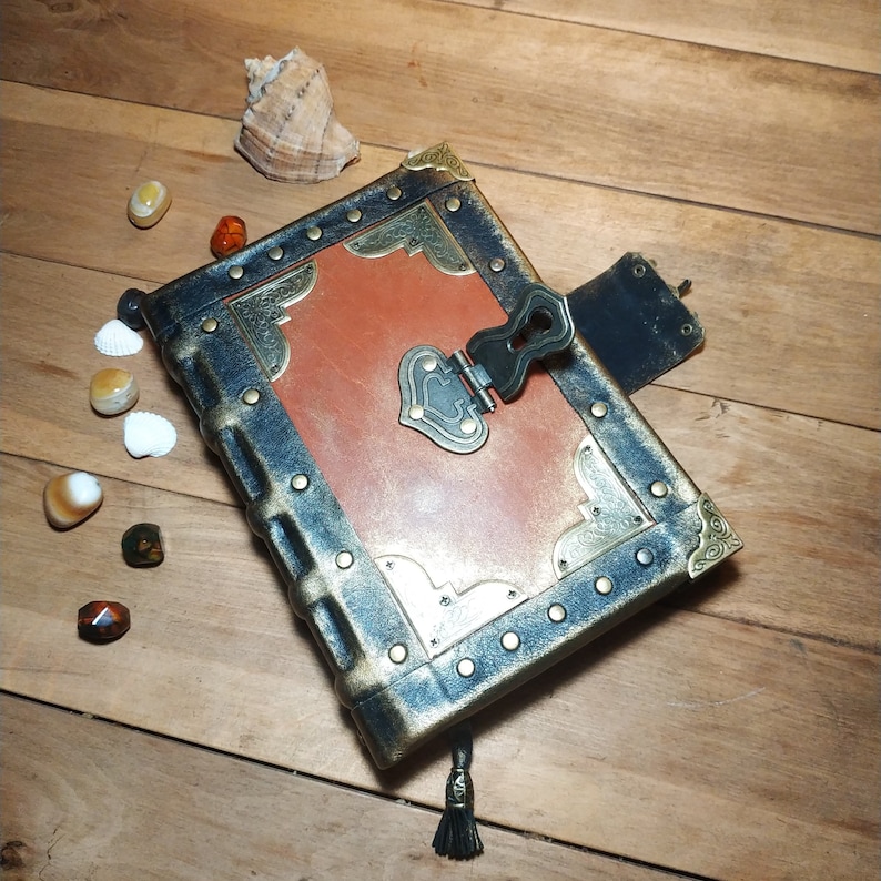 May include: A dark brown leather journal with a metal clasp and decorative accents. The journal has a distressed look and is adorned with gold and brass accents.