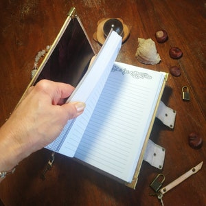 May include: A leather-bound journal with a gold clasp and decorative details. The journal is open to reveal lined pages and a decorative border.