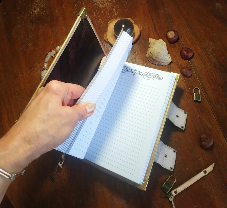 May include: A leather-bound journal with a gold clasp and decorative details. The journal is open to reveal lined pages and a decorative border.