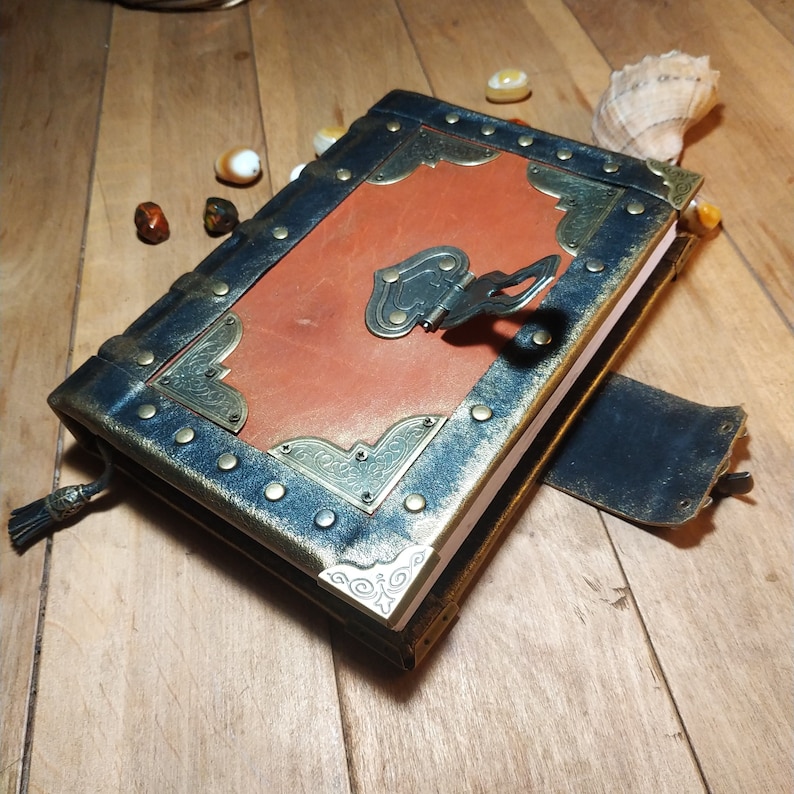May include: A brown leather journal with a black cover and gold accents. The journal has a metal clasp and a decorative design on the front.