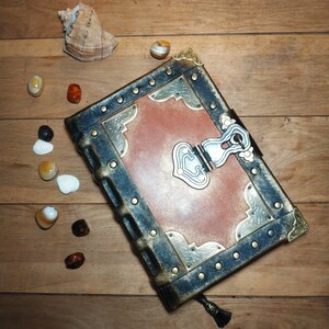 May include: A brown leather-bound journal with a metal clasp and decorative accents. The journal has a distressed look and is adorned with gold and silver embellishments.