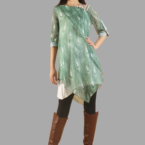 Op de afbeelding: Een groene en blauwe geprinte tuniek met een gelaagd ontwerp en een lange, asymmetrische zoom. De tuniek wordt gedragen met een zwarte legging en bruine laarzen tot op de knie.