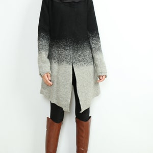 Puede incluir: Un abrigo largo de color negro y gris degradado con un cuello grande y un dobladillo largo y asimétrico. El abrigo se lleva sobre leggings negros y botas marrones de caña alta.