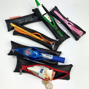 Könnte beinhalten: Vier schwarze Reißverschlusstaschen aus recycelten Schläuchen, jede mit einem anderen Reißverschluss in einer anderen Farbe und einem anderen Gegenstand im Inneren. Die Taschen sind mit roten Nähten gefüttert. Die Gegenstände in den Taschen sind ein Bleistift, ein Nasenspray, ein rosa Lippenbalsam und ein blauer Stift.