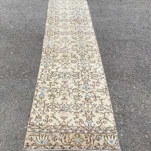 May include: A vintage cream-colored runner rug with a floral pattern in shades of brown and blue. The rug has a fringed edge.