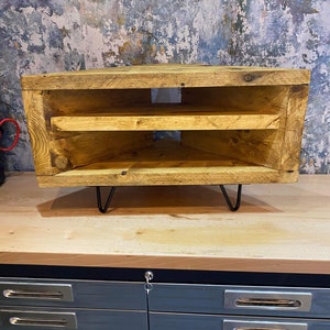 K&ouml;nnte beinhalten: Rustikale TV-Konsole aus Holz mit nat&uuml;rlichem Finish. Die Konsole hat zwei offene Regale und steht auf schwarzen Haarnadelbeinen. Die Holzmaserung ist sichtbar. Die Konsole ist etwa 76 cm breit.