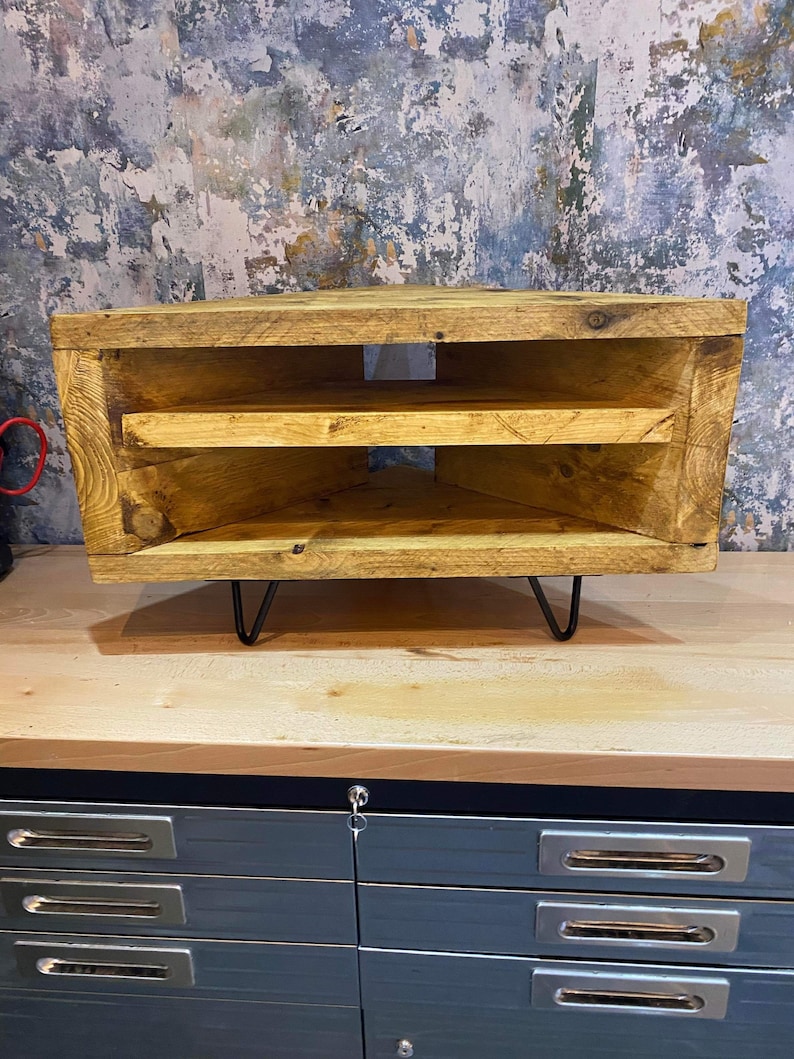 K&ouml;nnte beinhalten: Rustikale TV-Konsole aus Holz mit nat&uuml;rlichem Finish. Die Konsole hat zwei offene Regale und steht auf schwarzen Haarnadelbeinen. Die Holzmaserung ist sichtbar. Die Konsole ist etwa 76 cm breit.