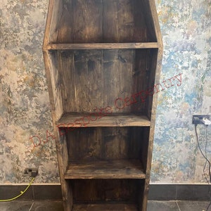 Op de afbeelding: Een handgemaakt, doodskistvormig boekenrek van donker gebeitst hout. Het boekenrek heeft drie planken en is ontworpen met een unieke, gotische esthetiek. De tekst "D.A. Bespoke Carpentry" is zichtbaar.