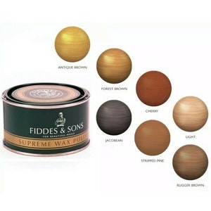 K&ouml;nnte beinhalten: Eine Dose Fiddes & Sons Supreme Wax Polish mit gr&uuml;n-goldener Beschriftung. Das Bild zeigt Holzkugeln in verschiedenen Farben: Antique Brown, Forest Brown, Cherry, Light, Jacobean, Stripped Pine und Rugger Brown.