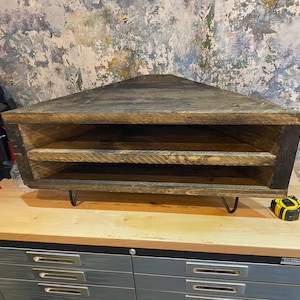 K&ouml;nnte beinhalten: Rustikales, dreieckiges Eckregal aus dunkel gebeiztem Holz. Es hat zwei Innenb&ouml;den und wird von schwarzen Haarnadelbeinen getragen. Das Regal ist so konzipiert, dass es perfekt in eine Ecke passt und Platz spart.
