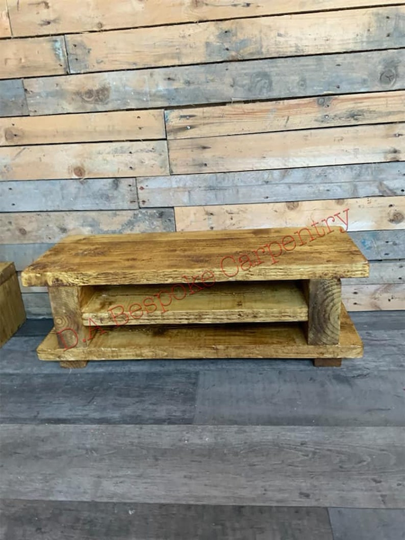 Op de afbeelding: Een rustieke houten salontafel met twee planken. De tafel is gemaakt van lichtbruin hout en heeft een natuurlijke, verweerde uitstraling. De tekst "Bespoke Carpentry" is zichtbaar op de bovenkant van de tafel.