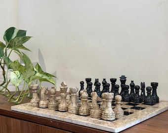 May include: A marble chess set with black and white pieces on a marble board. The pieces are arranged in a starting position. The board is on a wooden surface.