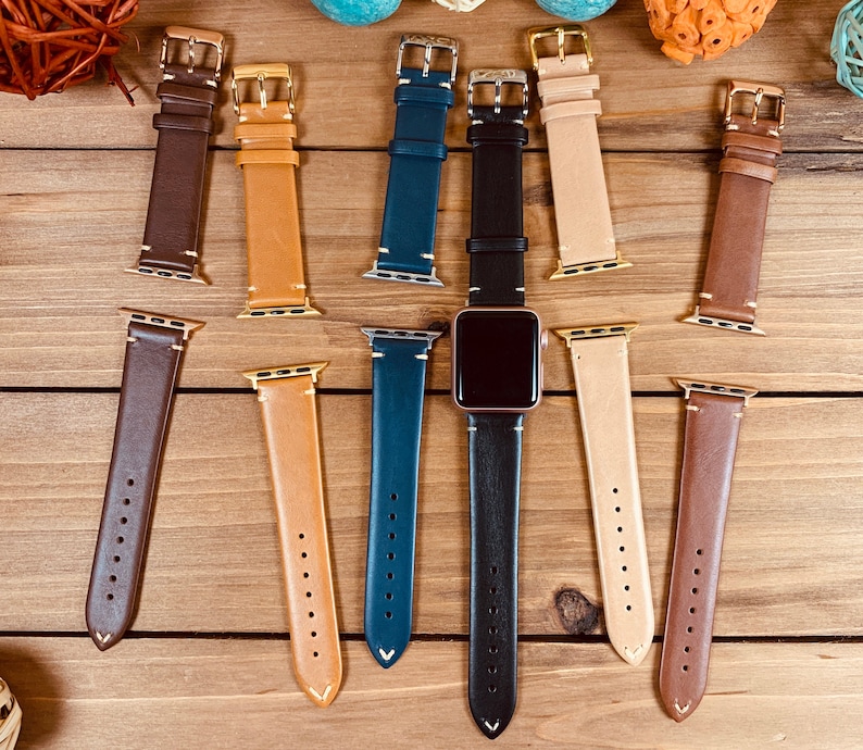 May include: Assortment of leather watch bands in various colors, including brown, tan, black, and blue. The bands are all made of leather and have a stitched design. The bands are shown on a wooden surface.