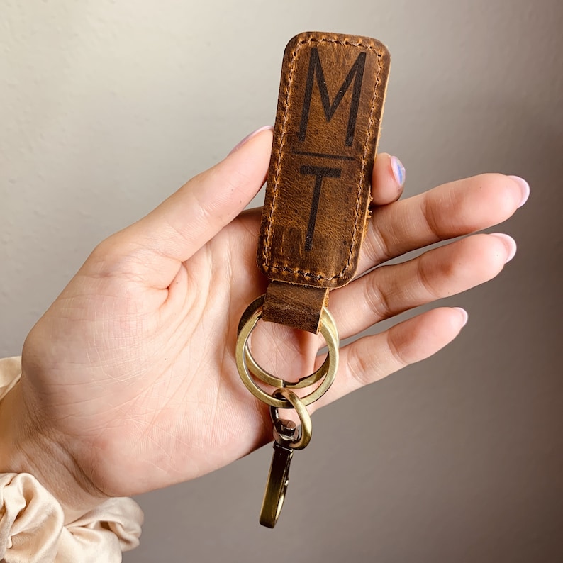 a hand holding a leather keychain with the letter m on it