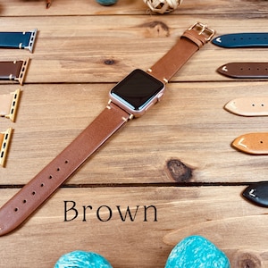 May include: A brown leather Apple Watch band with a rose gold Apple Watch on a wooden surface. The band is shown with other leather bands in different colors.