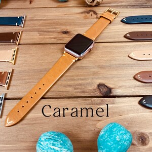 May include: Caramel leather Apple Watch band with a gold buckle. The band is shown on a wooden surface with other leather bands in different colors.