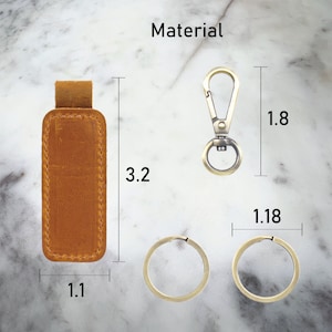 May include: A brown leather key chain with a metal clasp and two metal rings. The key chain measures 3.2 inches in length, 1.1 inches in width, and 1.8 inches in height.