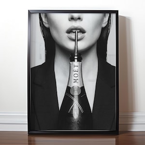 Puede incluir: Impresión en blanco y negro enmarcada que muestra a una persona con una botella de champán en la boca. La botella, con la etiqueta "MOET", está entre los labios. La persona lleva una blazer negro.