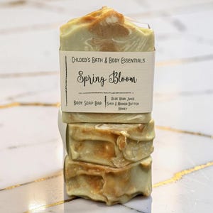 Könnte beinhalten: Ein Stapel aus drei rechteckigen Körperseifenstücken mit einer marmorierten hellgrünen und beigen Optik. Das oberste Stück trägt ein Papieretikett mit der Aufschrift Chloeb's Bath & Body Essentials, Spring Bloom, Body Soap Bar, Aloe Vera Juice, Shea & Mango Butter, Honey.