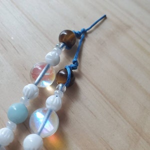 May include: A multi-strand beaded bracelet with blue, white, and brown beads. The bracelet is tied with a blue cord and has a knot at the end.