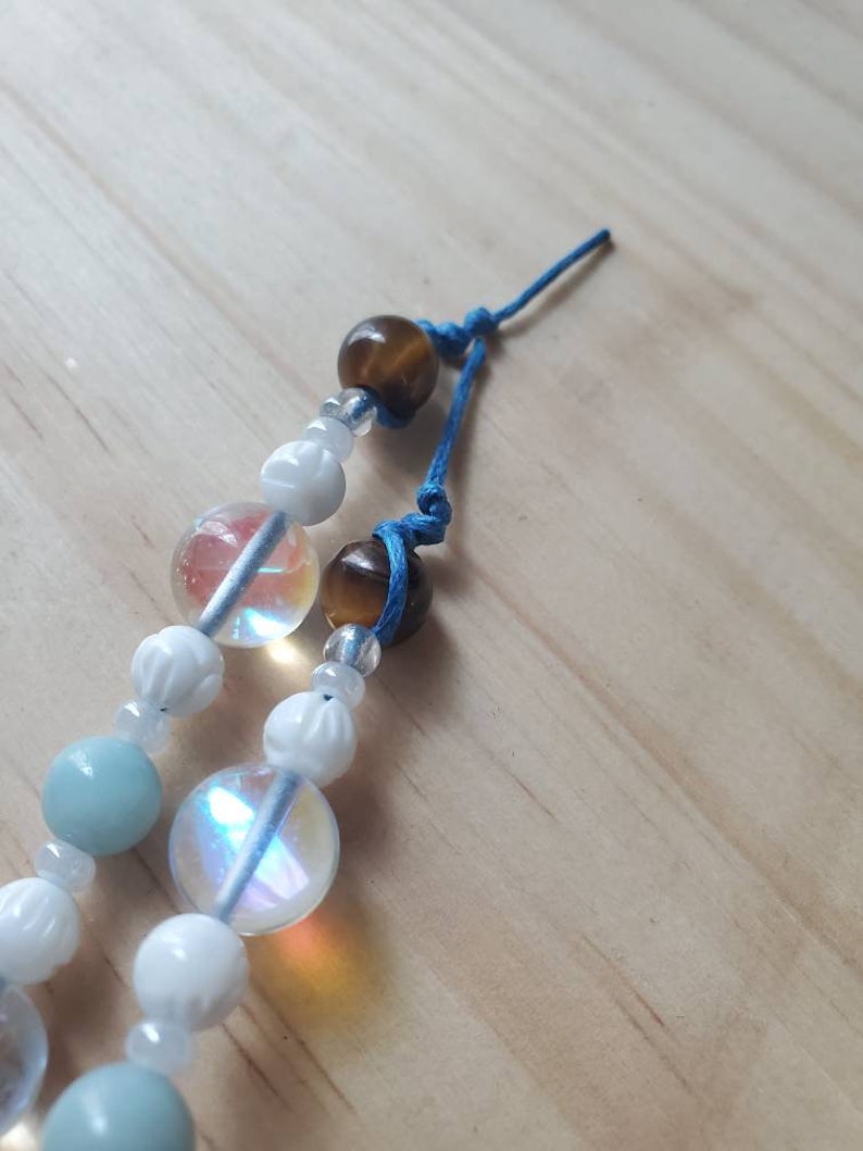 May include: A multi-strand beaded bracelet with blue, white, and brown beads. The bracelet is tied with a blue cord and has a knot at the end.