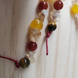 Op de afbeelding: Een close-up van een kralenarmband met rode, gele en bruine kralen. De armband is vastgebonden met rood touw.