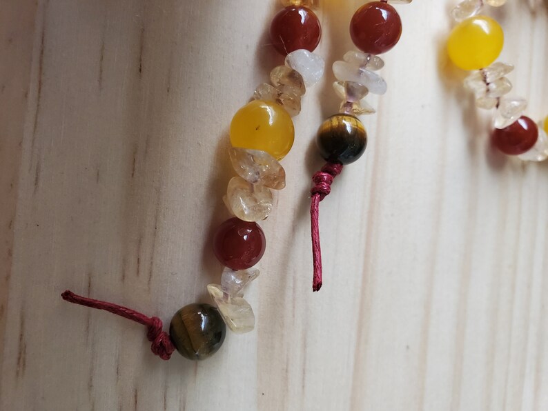 Op de afbeelding: Een close-up van een kralenarmband met rode, gele en bruine kralen. De armband is vastgebonden met rood touw.