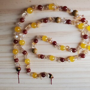 May include: A long necklace made of yellow, orange, and red gemstone beads. The necklace is made of various sizes and shapes of beads, including some small, irregular pieces. The necklace has two tiger's eye beads at the ends.