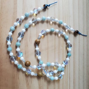May include: A multi-strand beaded necklace with white, light blue, and brown beads. The necklace is made of various types of stones and has a knotted closure.