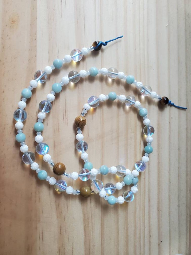 May include: A multi-strand beaded necklace with white, light blue, and brown beads. The necklace is made of various types of stones and has a knotted closure.