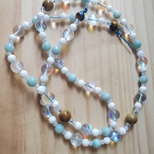 May include: A multi-strand necklace with white, light blue, and brown beads. The necklace is made of various types of stones, including clear quartz, aquamarine, and tiger's eye.