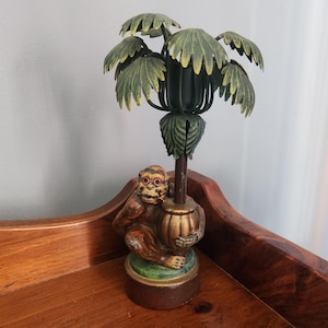 May include: A vintage decorative lamp featuring a monkey holding a barrel, with a palm tree-shaped top. The lamp has a brown base, green and gold accents, and a detailed monkey figurine. The palm leaves are green and yellow.