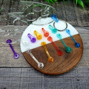 May include: A set of colorful plastic keychains in various shades of blue, green, orange, yellow, and purple. The keychains are arranged on a wooden and white surface.