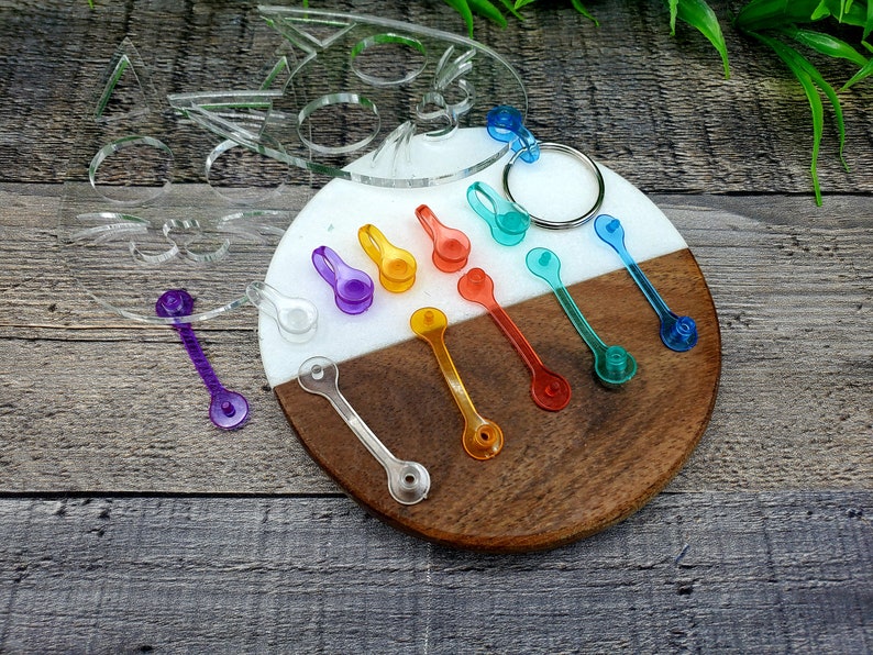 May include: A set of colorful plastic keychains in various shades of blue, green, orange, yellow, and purple. The keychains are arranged on a wooden and white surface.