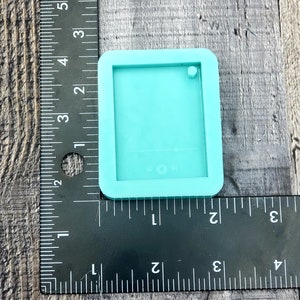 Puede incluir: Un molde de silicona turquesa para hacer manualidades de resina. El molde tiene forma de rect&aacute;ngulo con esquinas redondeadas y tiene un peque&ntilde;o agujero en la parte superior. El molde mide 3,8 cm de ancho y 5 cm de largo.