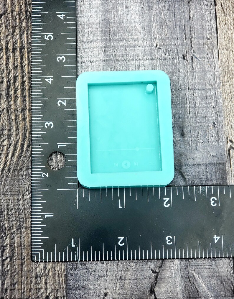 Puede incluir: Un molde de silicona turquesa para hacer manualidades de resina. El molde tiene forma de rect&aacute;ngulo con esquinas redondeadas y tiene un peque&ntilde;o agujero en la parte superior. El molde mide 3,8 cm de ancho y 5 cm de largo.