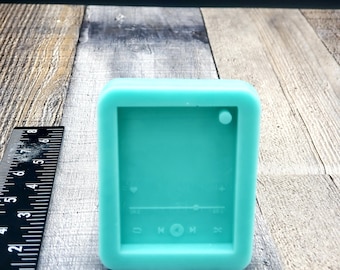May include: A teal blue silicone mold shaped like a music player with buttons for play, pause, and skip. The mold has a heart icon, a slider, and a plus sign.