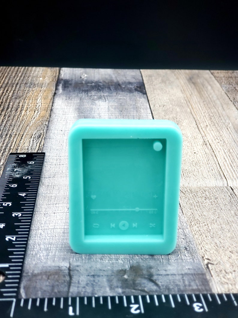 Puede incluir: Un molde de silicona azul turquesa con forma de reproductor de m&uacute;sica con botones para reproducir, pausar y saltar. El molde tiene un icono de coraz&oacute;n, un control deslizante y un signo m&aacute;s.