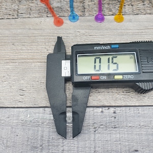 May include: A black digital caliper measuring a clear plastic object. The caliper reads 0.15 inches.