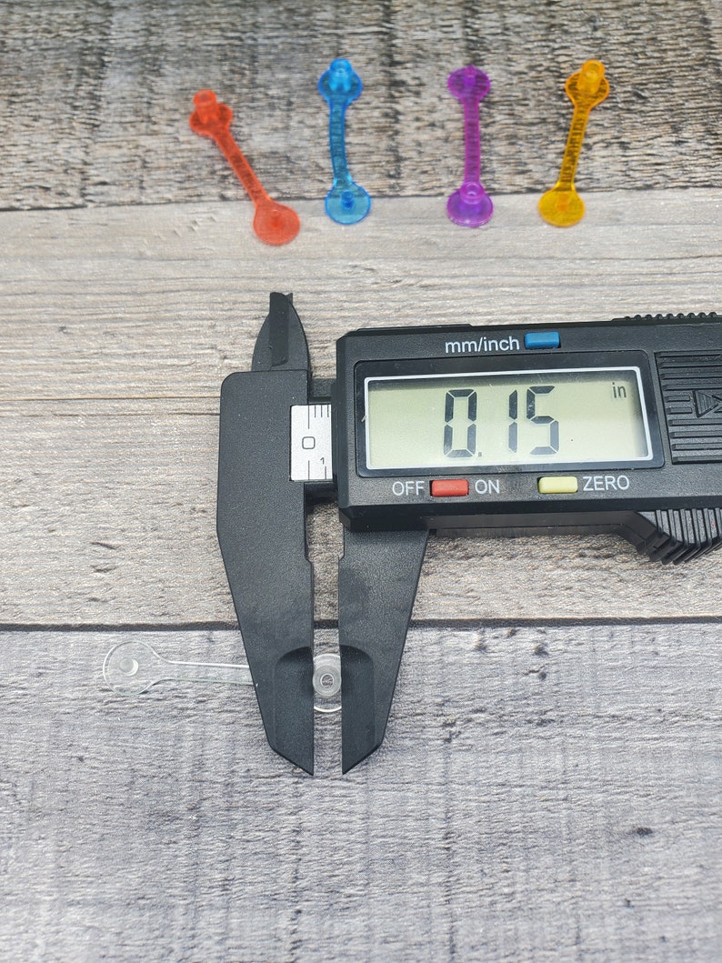 May include: A black digital caliper measuring a clear plastic object. The caliper reads 0.15 inches.