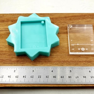 Puede incluir: Un molde de silicona turquesa con forma de estrella con un recorte rectangular en el centro. Tambi&eacute;n se muestra una plantilla de pl&aacute;stico transparente con un recorte rectangular y el texto "HON". Se puede ver una regla en la parte inferior de la imagen.