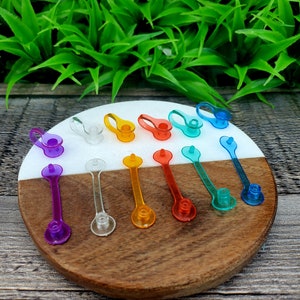 Może przedstawiać: Zestaw kolorowych plastikowych korków do butelek w różnych kształtach i rozmiarach. Korki są ułożone na biało-brązowej powierzchni drewnianej.