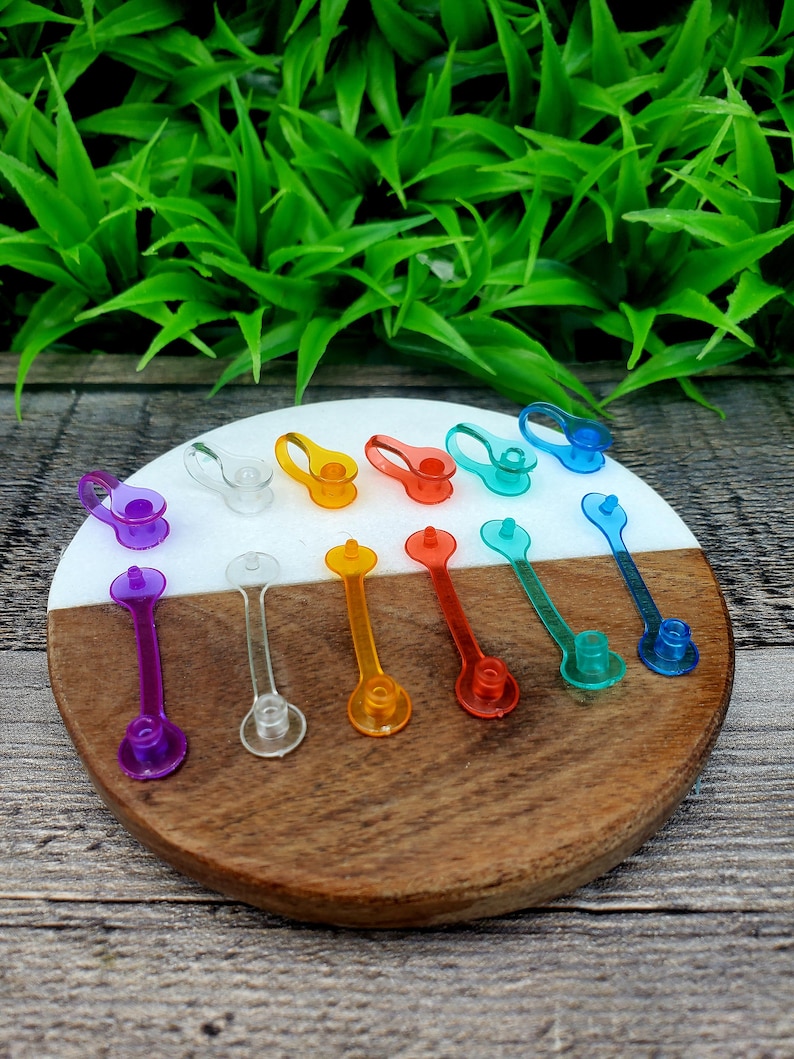 May include: Assortment of colorful plastic bottle stoppers in various shapes and sizes. The stoppers are arranged on a white and brown wooden surface.