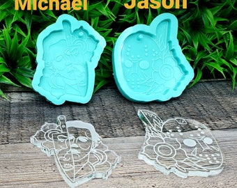 May include: Two teal blue silicone molds for making resin crafts. The molds are shaped like a human head with a knife and a hockey mask. The text "Michael" and "Jason" are written above the molds.