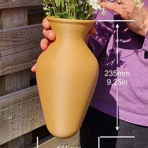 May include: A light brown ceramic vase with a textured surface, holding a bouquet of white flowers. The vase is 9.25 inches tall and 4.92 inches wide.