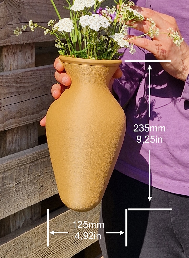 May include: A light brown ceramic vase with a textured surface, holding a bouquet of white flowers. The vase is 9.25 inches tall and 4.92 inches wide.