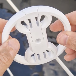 Peut inclure: Anneau en plastique blanc avec une ouverture centrale et deux ensembles de trois ouvertures plus petites de chaque côté. L'anneau est conçu pour être plié en deux.