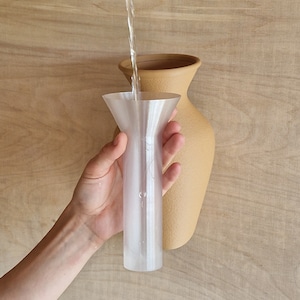 May include: A clear plastic funnel being used to pour water into a tan ceramic vase.