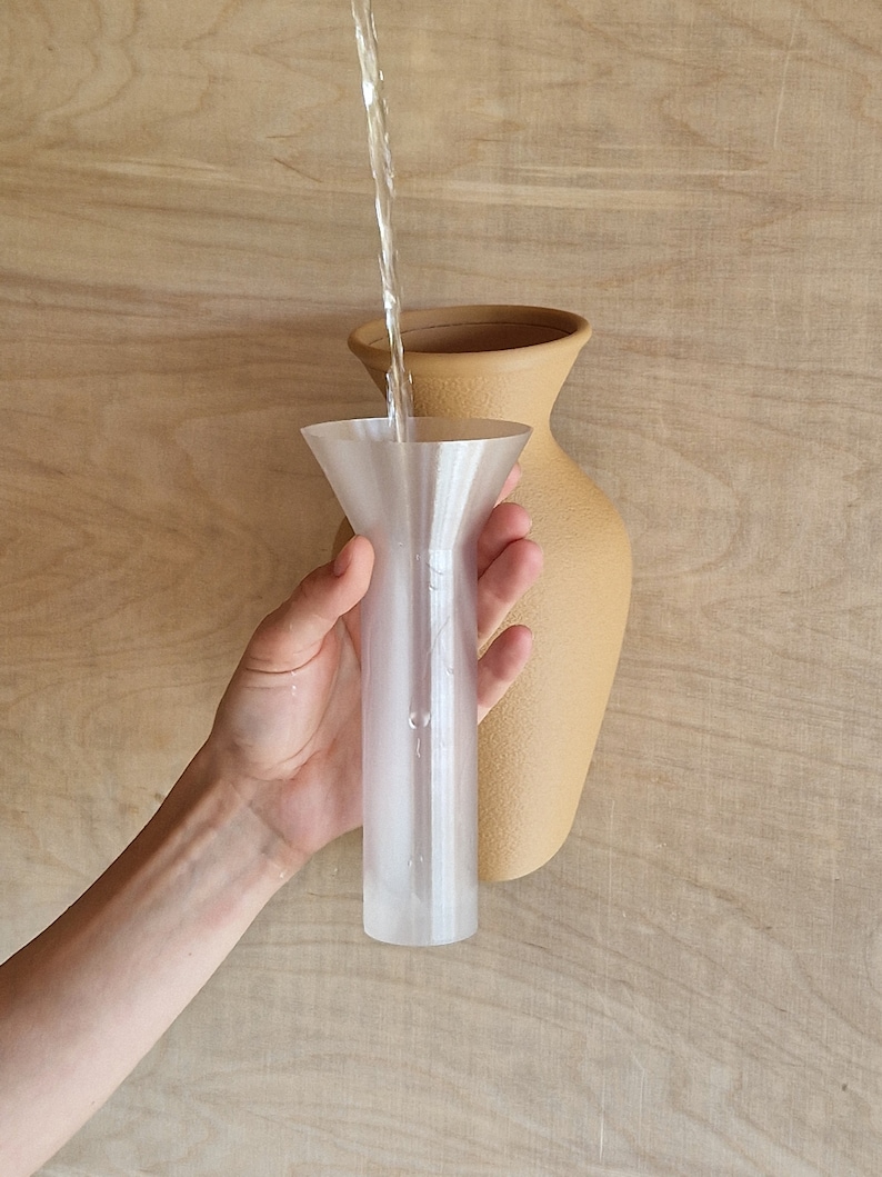 May include: A clear plastic funnel being used to pour water into a tan ceramic vase.