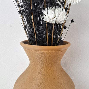 May include: A brown ceramic vase with a textured surface holds a bouquet of white dried flowers with black stems.